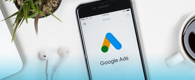 A smartphone with Google Ads app opened lying next to a cup of coffee and headphones.
