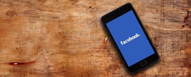 A smartphone with the facebook logo displayed on it lies on a wooden ground.